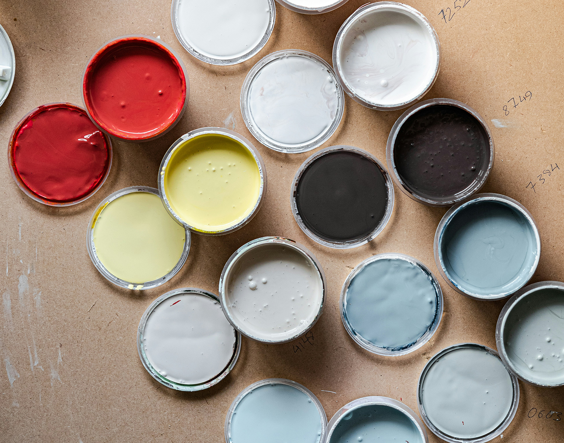 Open paint containers arranged on a table, showing various colors including red, yellow, gray, and blue.