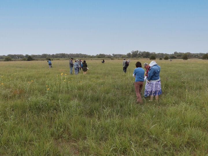 Otoe tribal members walking and standing in a grassy field under a cloudy sky
