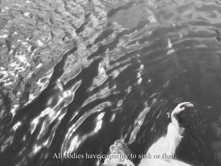 A person’s arm reaches above rippling water in grayscale.
