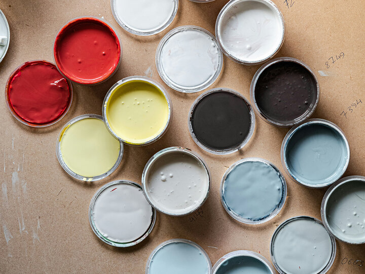 Open paint containers arranged on a table, showing various colors including red, yellow, gray, and blue.